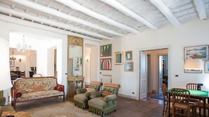 Un salón espacioso con techo alto, un sofá, sillones, una mesa de comedor y una araña.