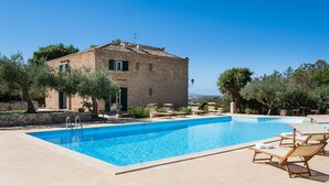 Una piscina con sillones de descanso, un edificio de piedra y vegetación circundante.