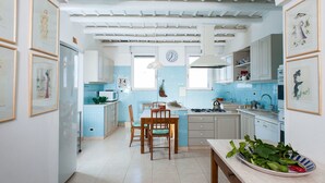 Una cocina con una mesa de comedor, sillas, un reloj y varios electrodomésticos.