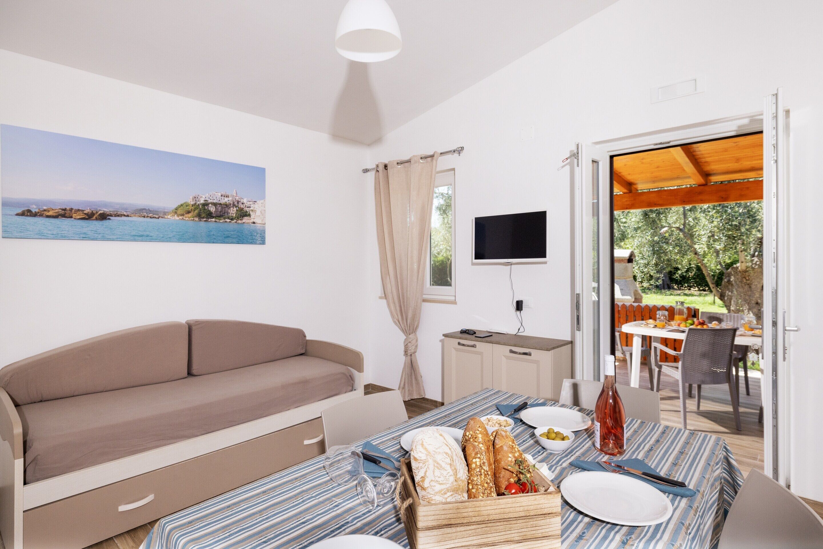 A room with a sofa, a dining table with food, a TV, and a view of the outdoors.