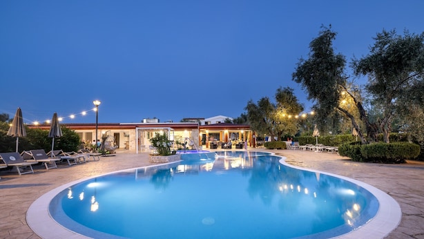 A swimming pool with lounge chairs and umbrellas, surrounded by trees and a building with a red roof. - Farmhouse in Vieste Near Gargano Coast (Vieste)