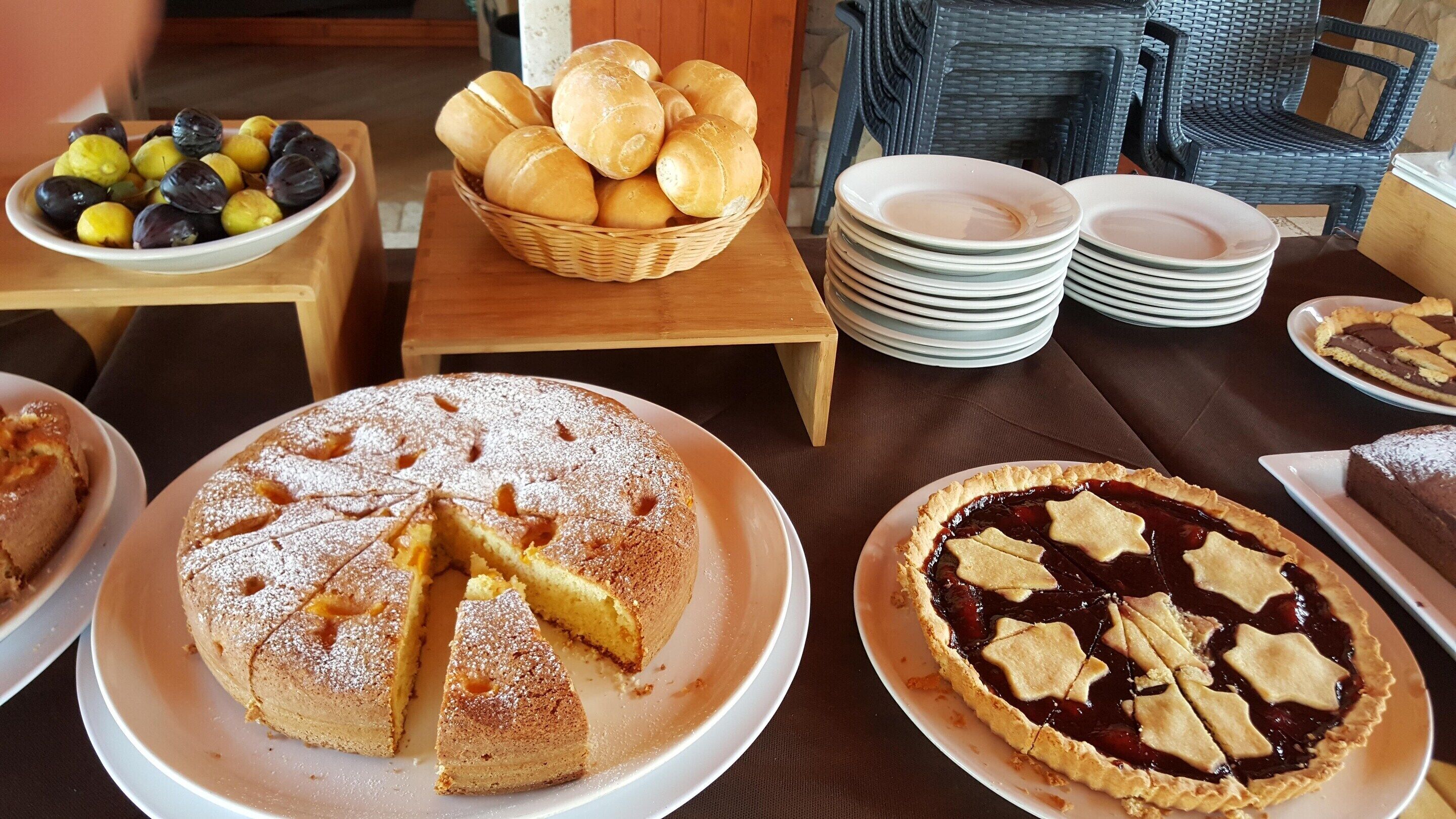 A dining table with various desserts, including a cake and a pie, plates, and a basket of bread.