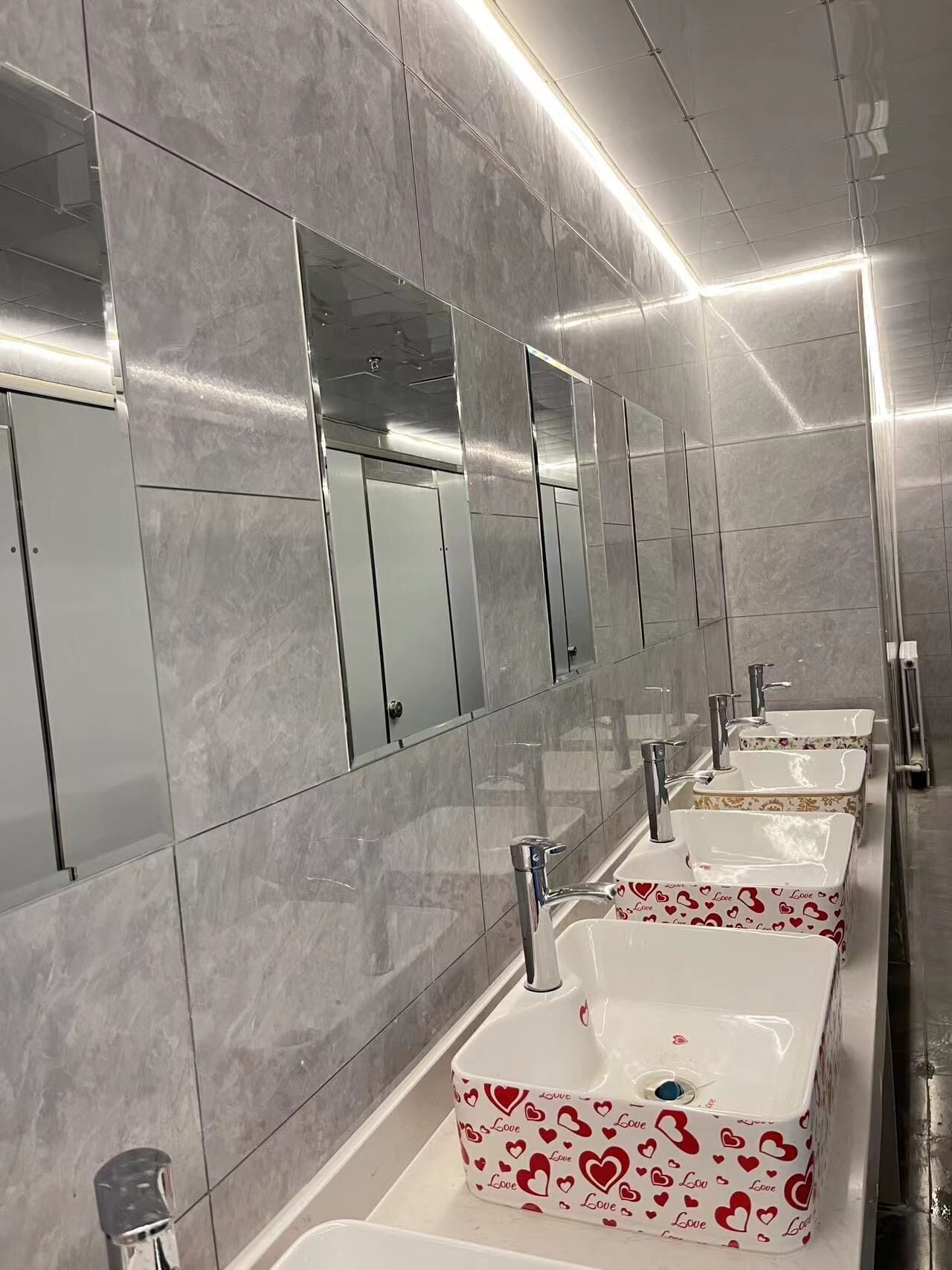 A modern bathroom with marble walls, multiple sinks, and mirrors.