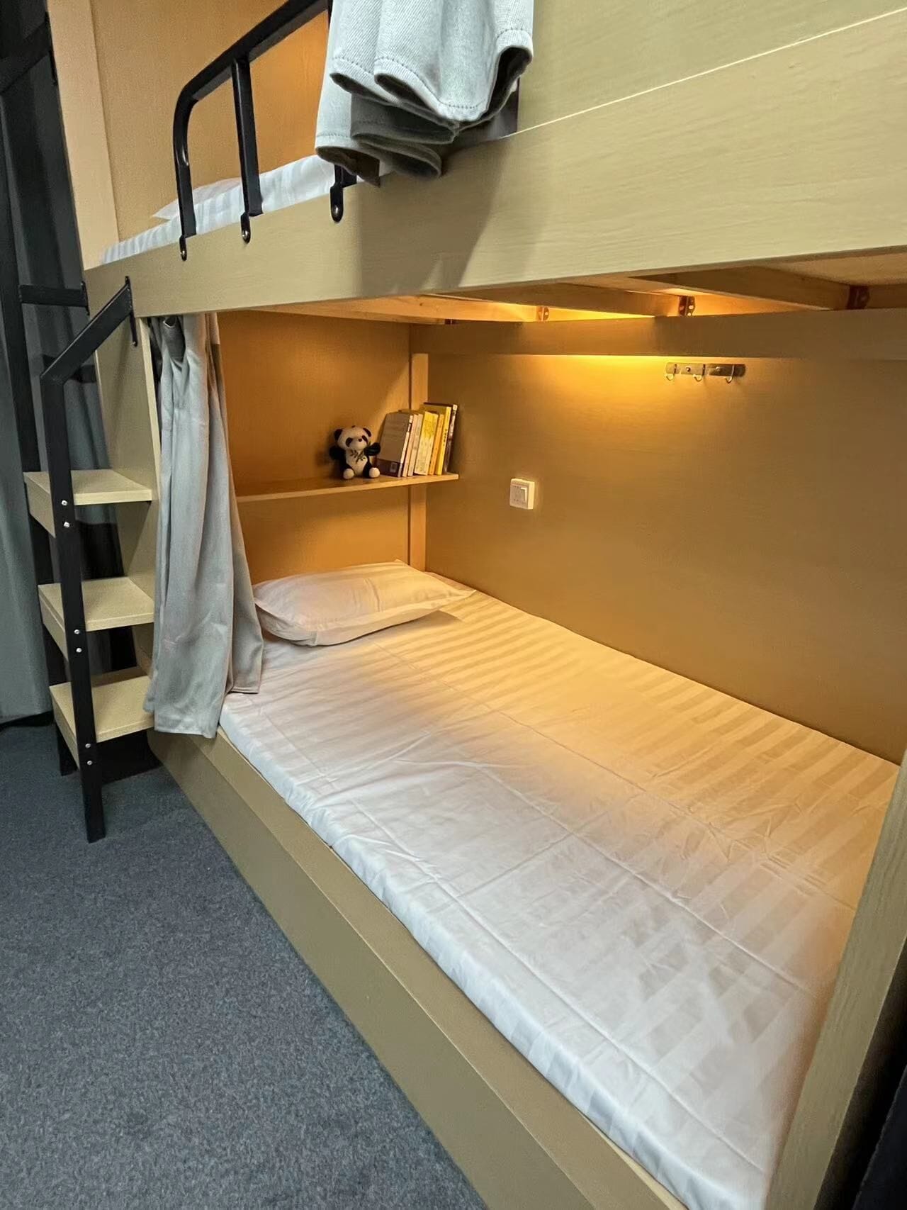 A bunk bed with a ladder, a shelf with books and a small panda figurine, and a curtain.
