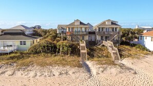 Una propiedad frente a la playa con varias casas, una playa de arena y una escalera que lleva a un balcón.
