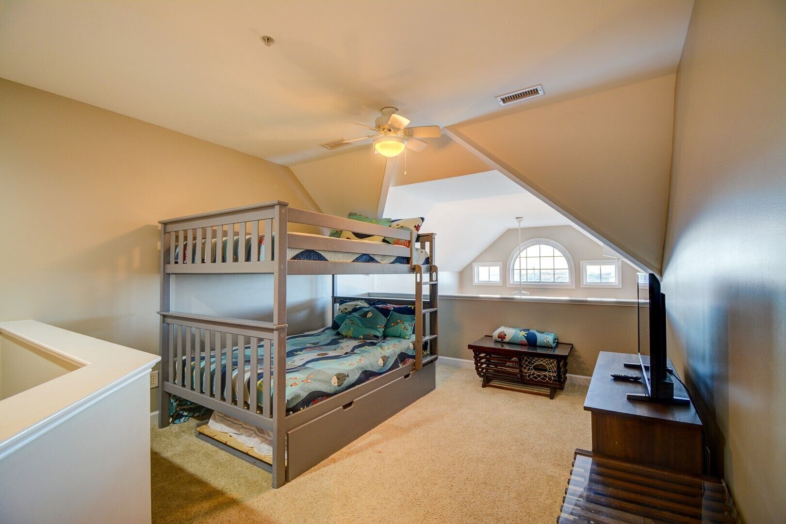 A bedroom with a bunk bed, a desk, a chair, a ceiling fan, and a window.