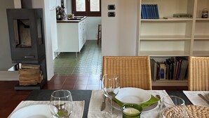 Un comedor con chimenea, una cocina al fondo y una estantería con libros y objetos decorativos.