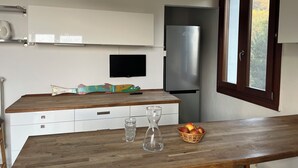 Una cocina con encimera de madera, un refrigerador, un televisor y un ventanal con vistas a árboles.