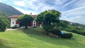 Una casa con fachada roja y blanca, rodeada de un césped cuidado y árboles.