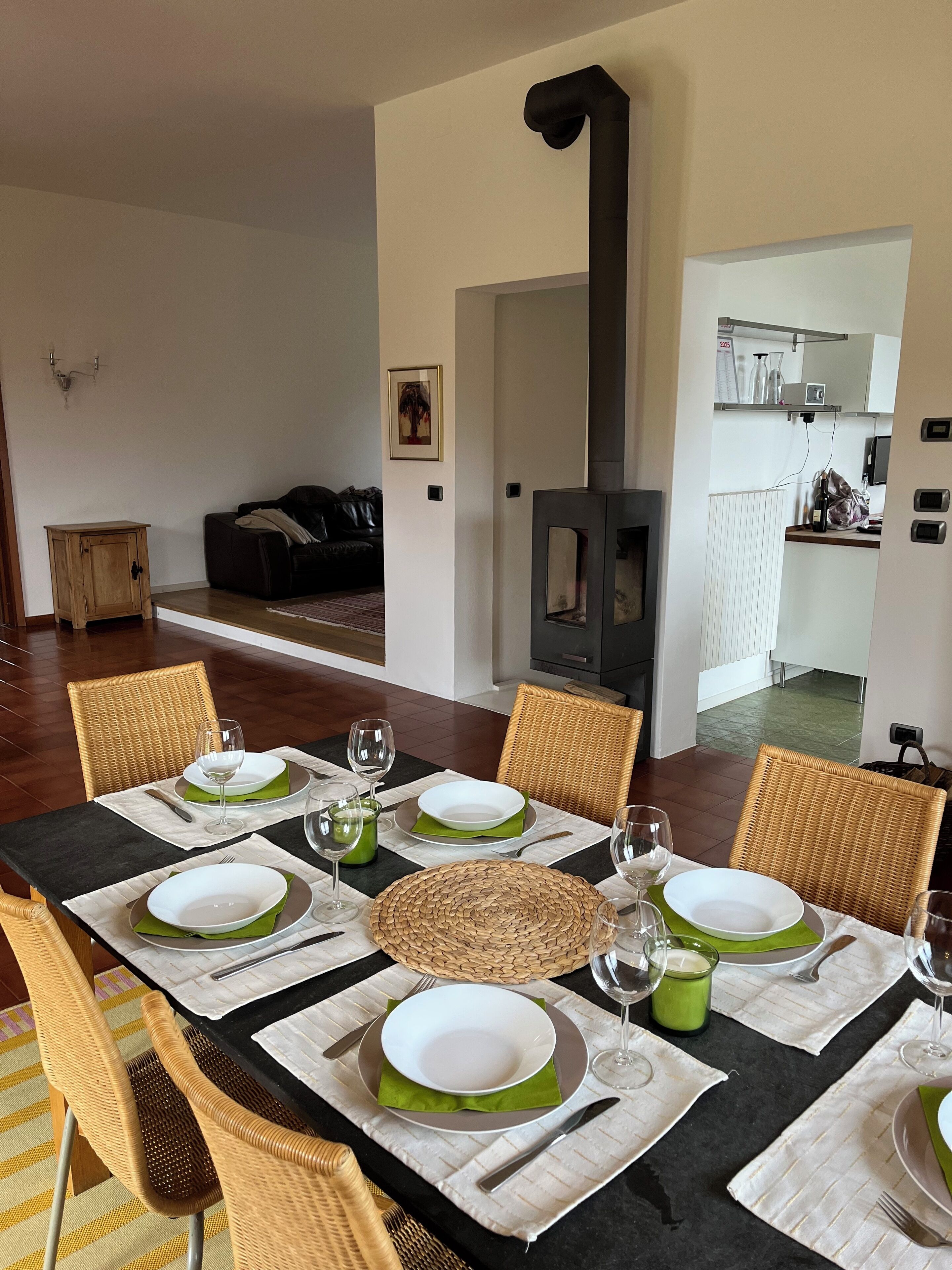 Un comedor con una mesa larga dispuesta para seis personas, rodeada de sillas de mimbre. Se observa una estufa de leña negra al fondo.