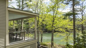 A covered deck with outdoor furniture overlooking a river, surrounded by trees. - Peaceful Riverfront Hideaway | 4BR/3BA | Wildlife, Views & Deep Water Dock (Edgecomb)