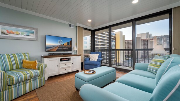 Een moderne woonkamer met gestreepte banken, een flatscreen televisie en een balkon met uitzicht op de stad.