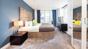 A modern hotel room with a large bed, a nightstand, a dresser, and a TV. - Koks Mews 2 Bed 2 Bath Apartment - ExCeL (London)