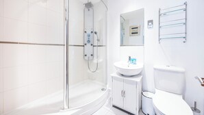 A modern bathroom with a glass-enclosed shower, a white sink, and a toilet. - Koks Mews 2 Bed 2 Bath Apartment - ExCeL (London)