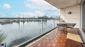 A balcony with a view of a river and city skyline, featuring a table and chairs. - Koks Mews 2 Bed 2 Bath Apartment - ExCeL (London)