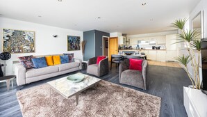 A modern living room with a grey sofa, a coffee table, and a dining area with a table and chairs. - Koks Mews 2 Bed 2 Bath Apartment - ExCeL (London)