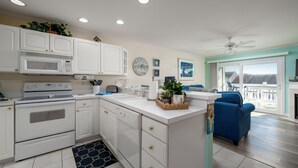 A modern kitchen with white cabinets, a microwave, and a stove. There is a blue chair and a plant on the counter.
