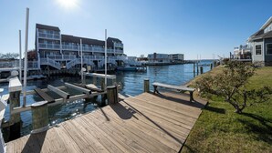 A waterfront property with a wooden dock, a multi-story building with balconies, and a clear view of the water.