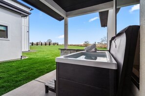 Una cocina al aire libre moderna con una parrilla integrada, un banco de concreto y vistas a un césped cuidado y árboles distantes.