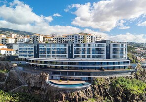 Un hotel moderno con varios pisos, una piscina y vistas del pueblo y las montañas circundantes.