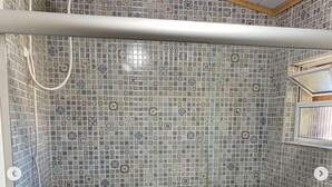 Un área de ducha con pared de azulejos, un cabezal de ducha manual y un box de ducha con mampara de cristal.