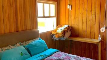 Una habitación de madera con una cama, una ventana y una estantería.