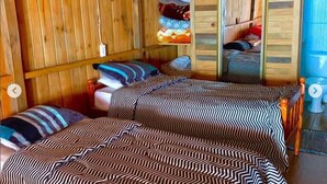 Una habitación con dos camas, paredes de madera y una litera al fondo.