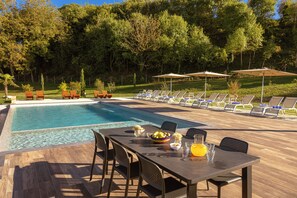 A poolside area with a table set for dining, lounge chairs, and umbrellas.