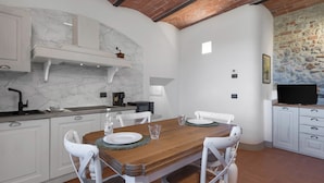 Zona pranzo con tavolo in legno, sedie bianche e cucina bianca con zoccolo in marmo.