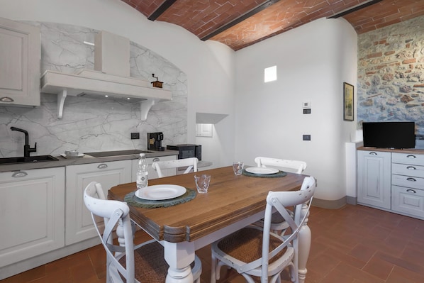A dining area with a wooden table, white chairs, and a white kitchen with marble backsplash.