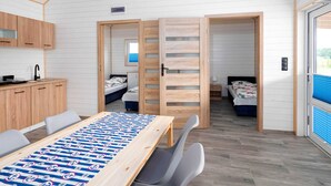 Una habitación moderna y funcional con una mesa de madera, dos camas, una kitchenette pequeña y una ventana con persianas.