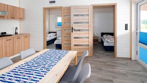 Una habitación moderna y funcional con una mesa de madera, dos camas, kitchenette y un ventanal amplio.
