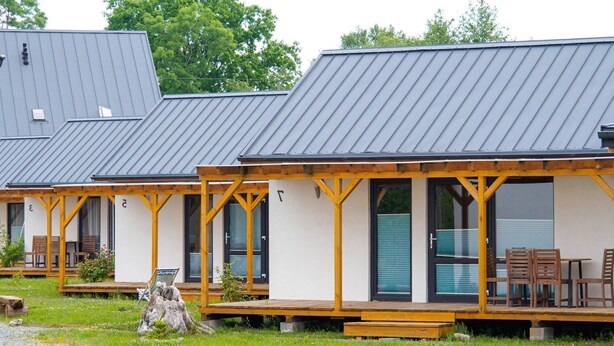 Filas de cabañas con terrazas de madera y ventanas amplias, ubicadas en una zona verde con un camino de grava.