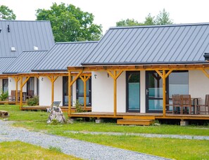 A row of cabins with wooden decks and large windows, set in a grassy area with a gravel path.