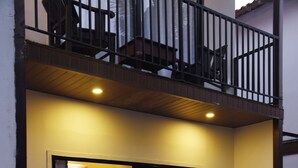 Ein zweigeschossiges Gebäude mit Balkon, einer kleinen Sitzgruppe im Freien inklusive Stühle und Tisch, sowie einem Blumentopf.