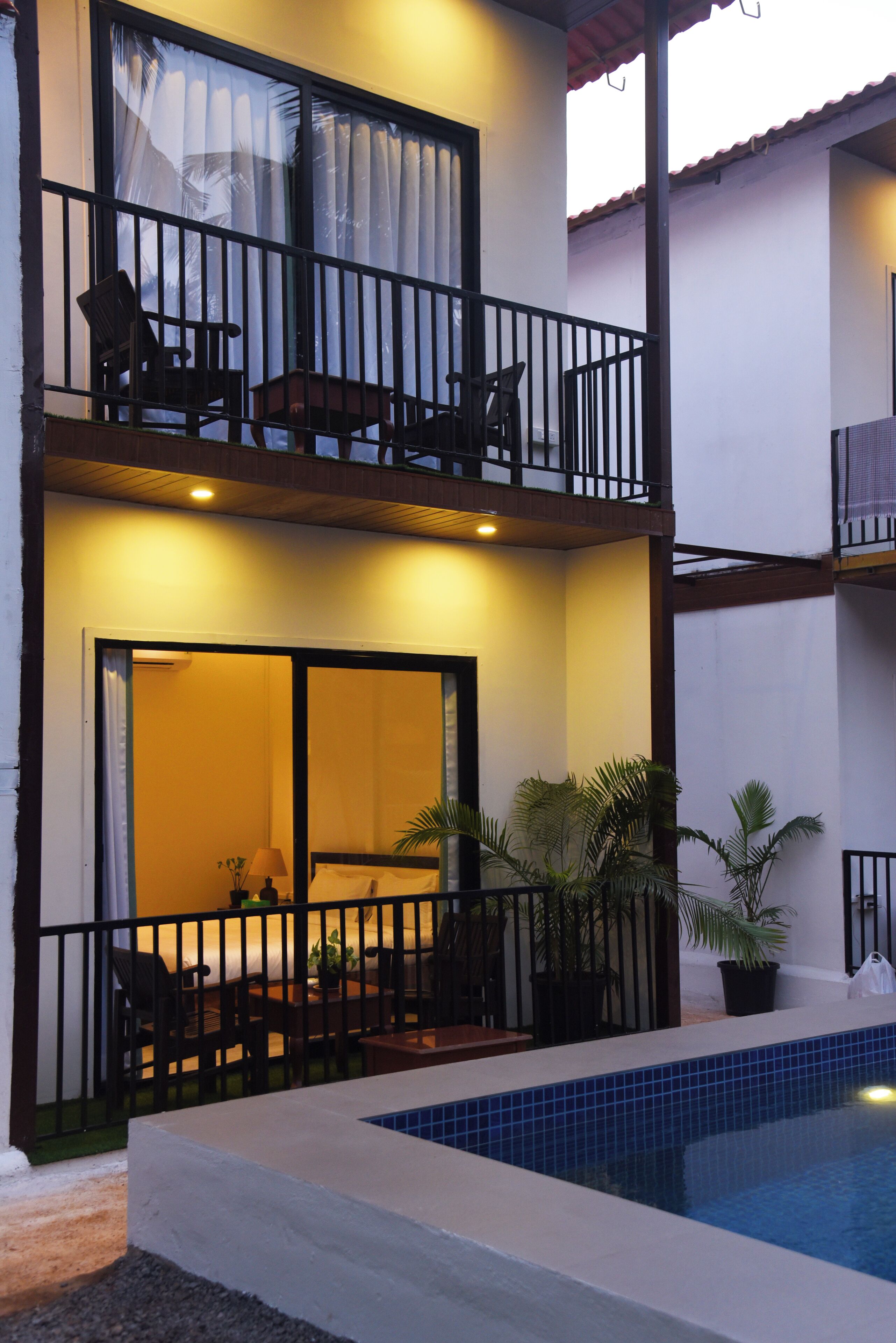A two-story building with a balcony, a pool, and a seating area with chairs and a table.