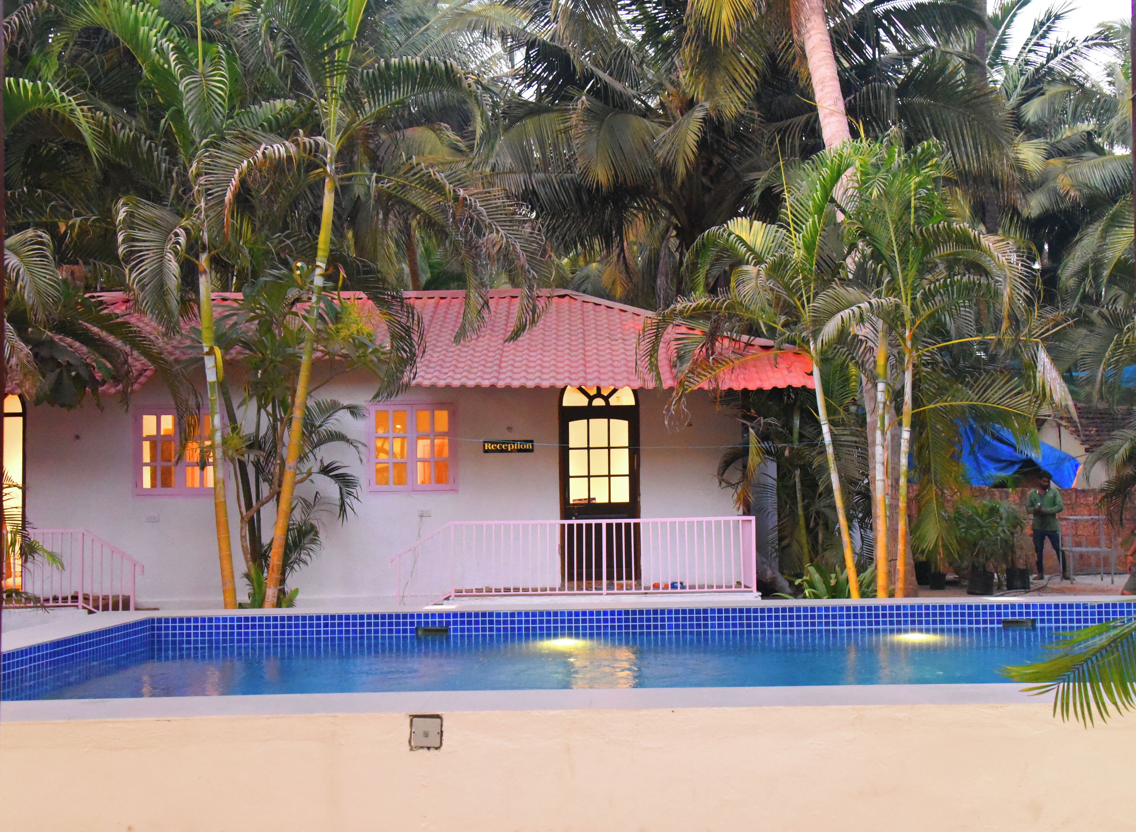 A poolside view of a building with a reception sign, surrounded by palm trees and a swimming pool.
