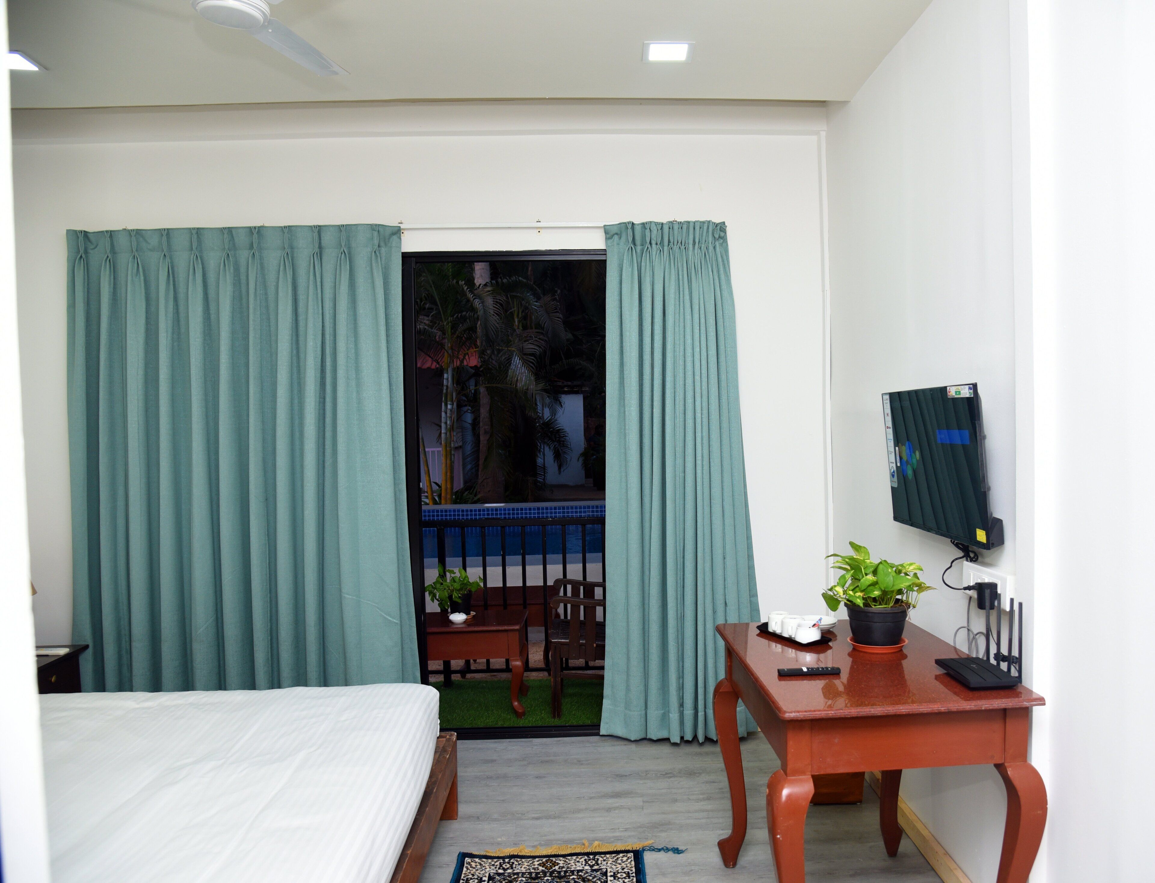 Quarto com cama, escrivaninha com planta e janela com cortinas.
