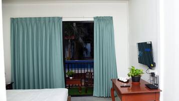 Quarto com cama, escrivaninha com planta e janela com cortinas.