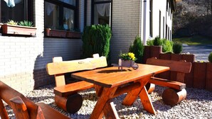 An outdoor seating area with a wooden table and benches, surrounded by potted plants and a brick wall.