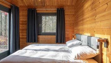 A wooden cabin bedroom with a large bed, a window with curtains, and a hanging light fixture.