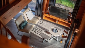 A cozy room with a wooden floor, a TV on a wooden stand, a small round table, and two chairs. - Lodge by the Lake in Arcen's Tranquil Nature (Arcen)