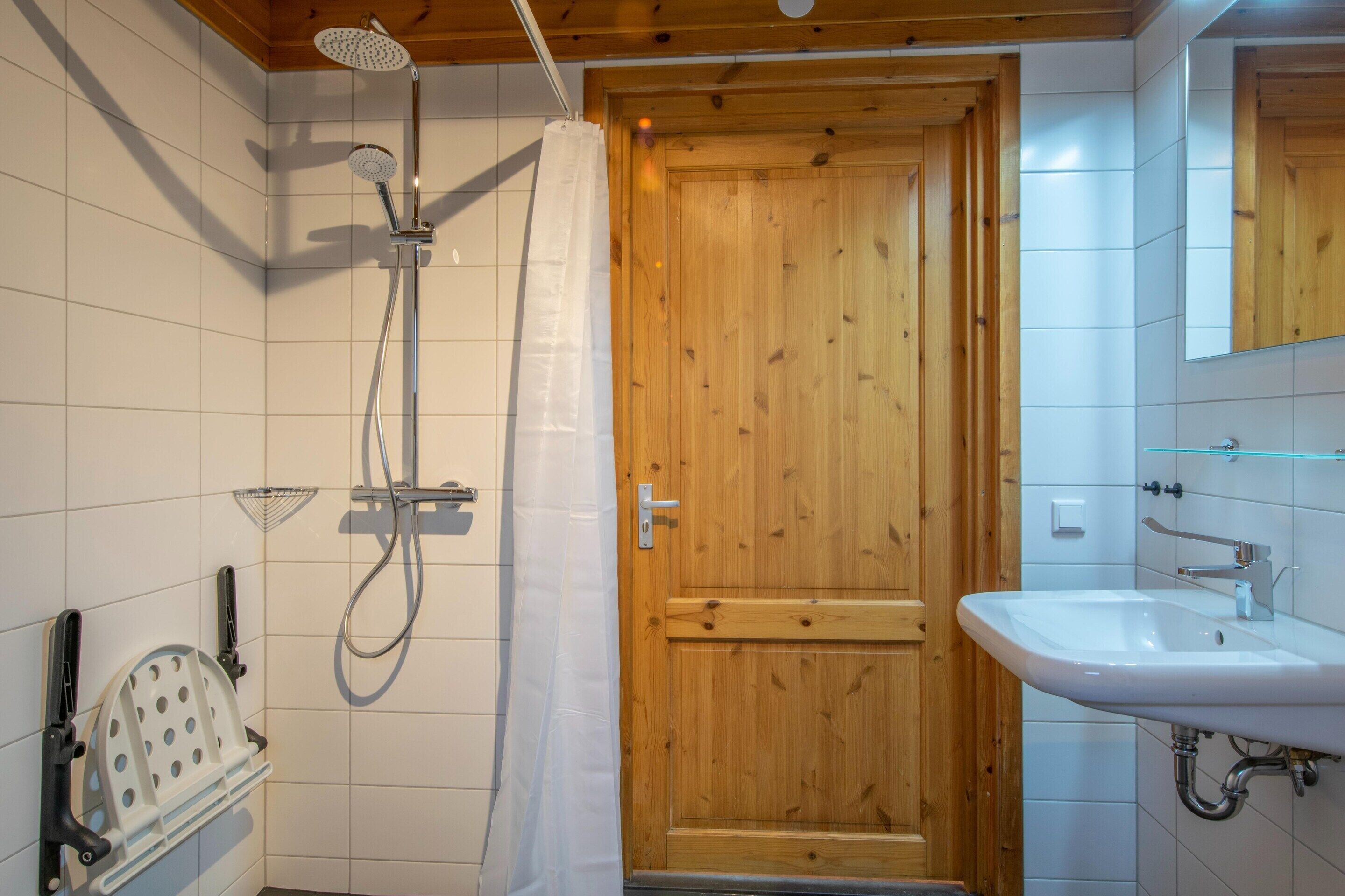 A bathroom with a wooden door, a shower with a handheld showerhead, a sink, and a mirror above it.