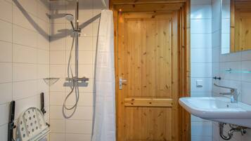 A bathroom with a wooden door, a shower with a handheld showerhead, a sink, and a mirror above it.