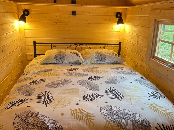 Quarto de cabana de madeira com cama, duas luminárias na parede e uma janela.