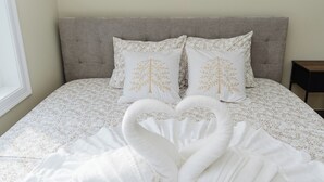 Un lit avec une tête de lit grise, une literie blanche ornée d’un motif de feuilles et deux oreillers décorés d’un motif d’arbre.