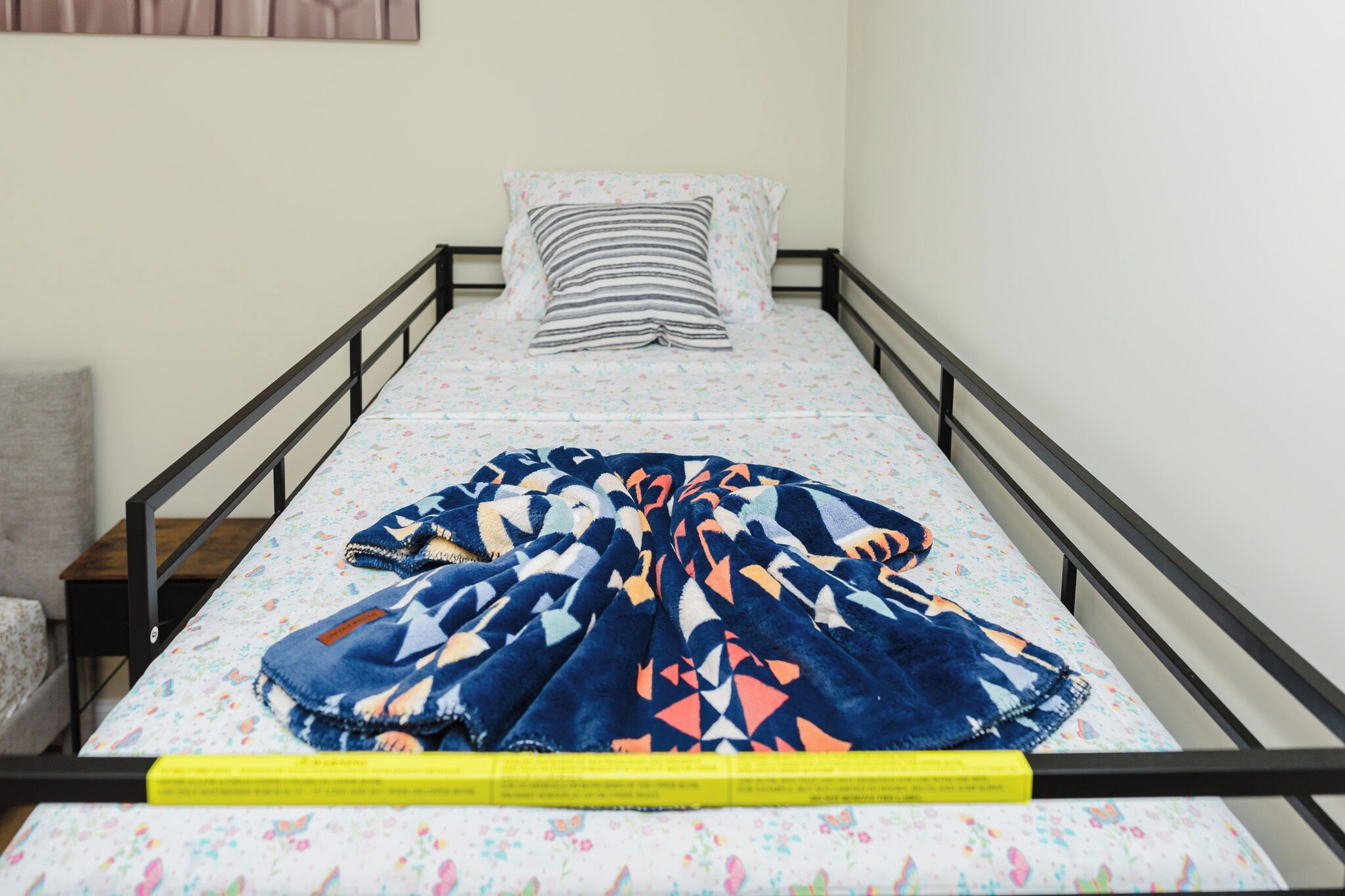 A single bed with a floral-patterned mattress, a blue and orange blanket, and a striped pillow.