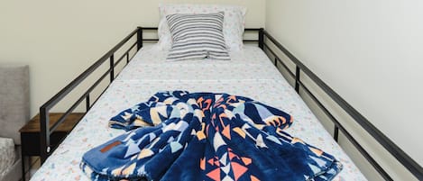 A single bed with a floral-patterned mattress, a blue and orange blanket, and a striped pillow.
