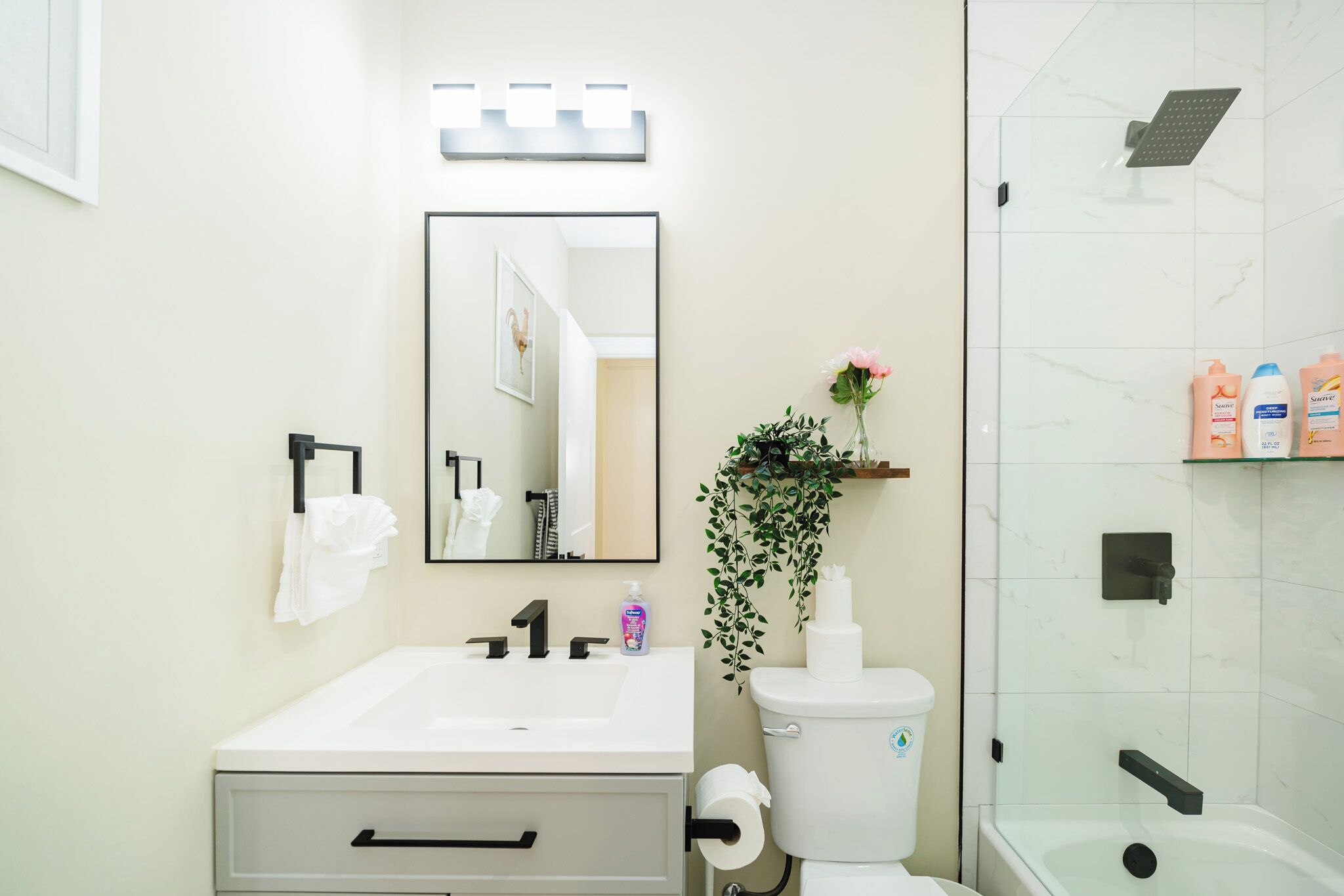 Un baño moderno con un lavamanos blanco, grifo negro y cabina de ducha de vidrio.