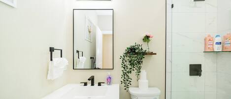 Un baño moderno con un lavamanos blanco, grifo negro y cabina de ducha de vidrio.